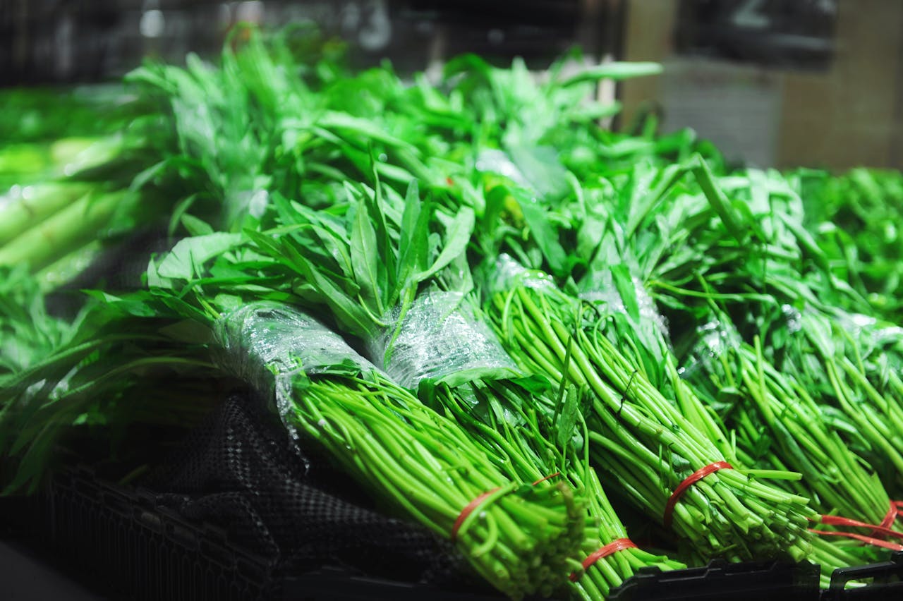 Close-up of fresh green vegetables neatly bundled with red ties at a market.